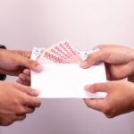 Hands exchanging an envelope with Indonesian Rupiah, highlighting financial transactions.