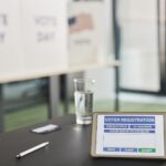 Tablet displaying digital voter registration at indoor voting station with vote day signs.