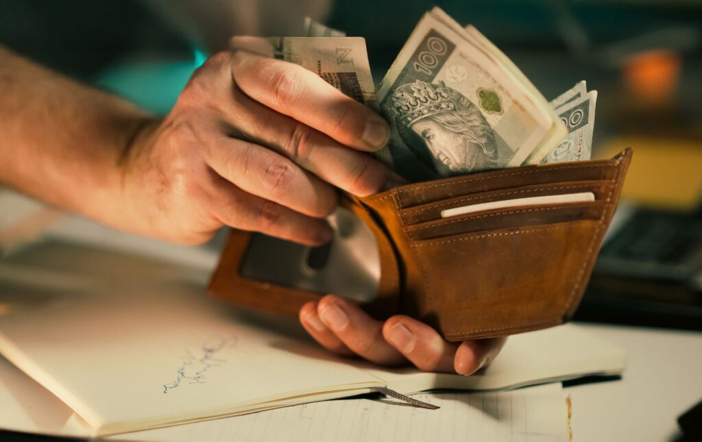 A close-up of hands holding a wallet filled with Polish banknotes on a desk.