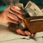 A close-up of hands holding a wallet filled with Polish banknotes on a desk.