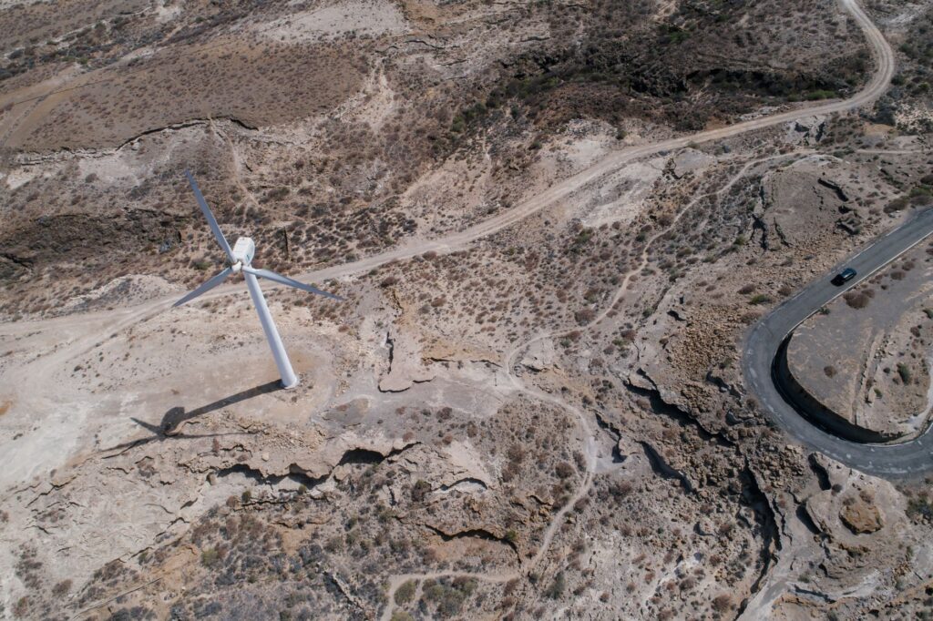 Drone shot capturing a wind turbine amidst a rugged desert landscape, showcasing sustainable energy.