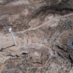 Drone shot capturing a wind turbine amidst a rugged desert landscape, showcasing sustainable energy.
