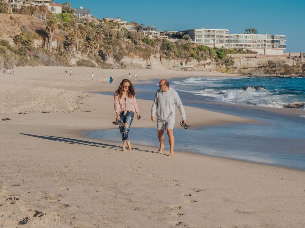 A senior couple walking barefoot along a picturesque sandy beach, enjoying a sunny day.