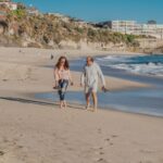A senior couple walking barefoot along a picturesque sandy beach, enjoying a sunny day.