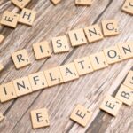Wooden letter tiles spell 'rising inflation' symbolizing economic concerns.