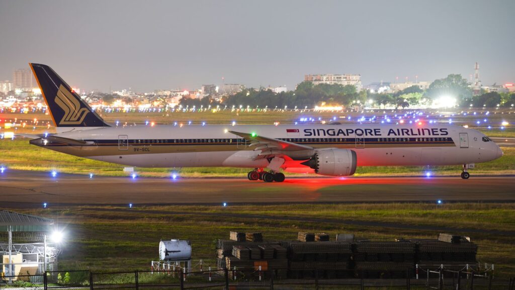 Singapore Airlines aircraft on runway at night with city lights in background.