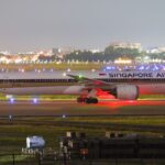 Singapore Airlines aircraft on runway at night with city lights in background.