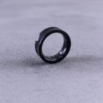 A modern black smart ring with visible circuitry resting on a textured concrete surface.