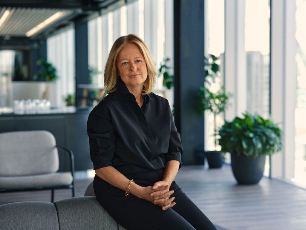 A confident woman seated in a modern office environment with natural light and greenery.