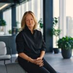A confident woman seated in a modern office environment with natural light and greenery.