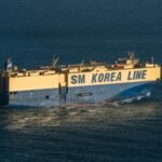 A large cargo ship, SM Korea Line, navigating through calm ocean waters under a clear blue sky.