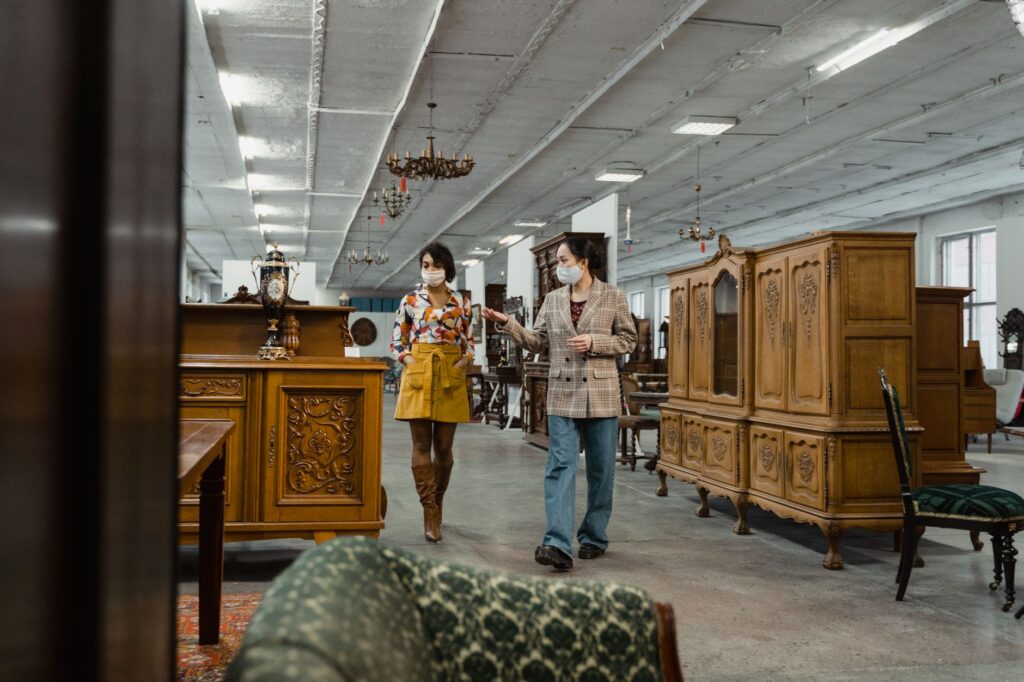 Two adults in masks browse antique furniture in a stylish vintage store.