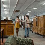 Two adults in masks browse antique furniture in a stylish vintage store.