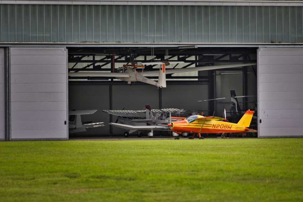 A vibrant yellow plane parked outside a hangar full of aircrafts on a sunny day.