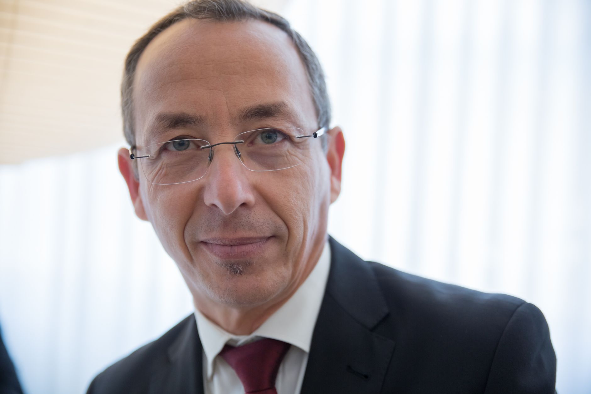 Close-up of a well-dressed businessman wearing glasses, smiling confidently indoors.