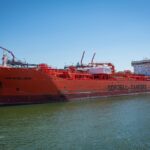 A large red oil tanker named Bow Excellence docked at a harbor under clear blue skies.