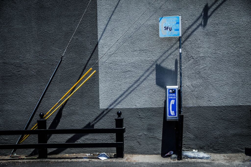 A vintage payphone beside a concrete wall in Los Angeles with striking shadows.