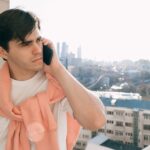 Young adult casually talking on the phone while enjoying a city view from a balcony.