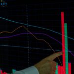 Hand pointing at a financial graph displaying cryptocurrency data analysis and trends.