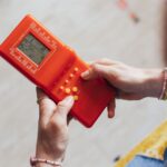 Hands holding a retro red handheld game console, playing a classic game.