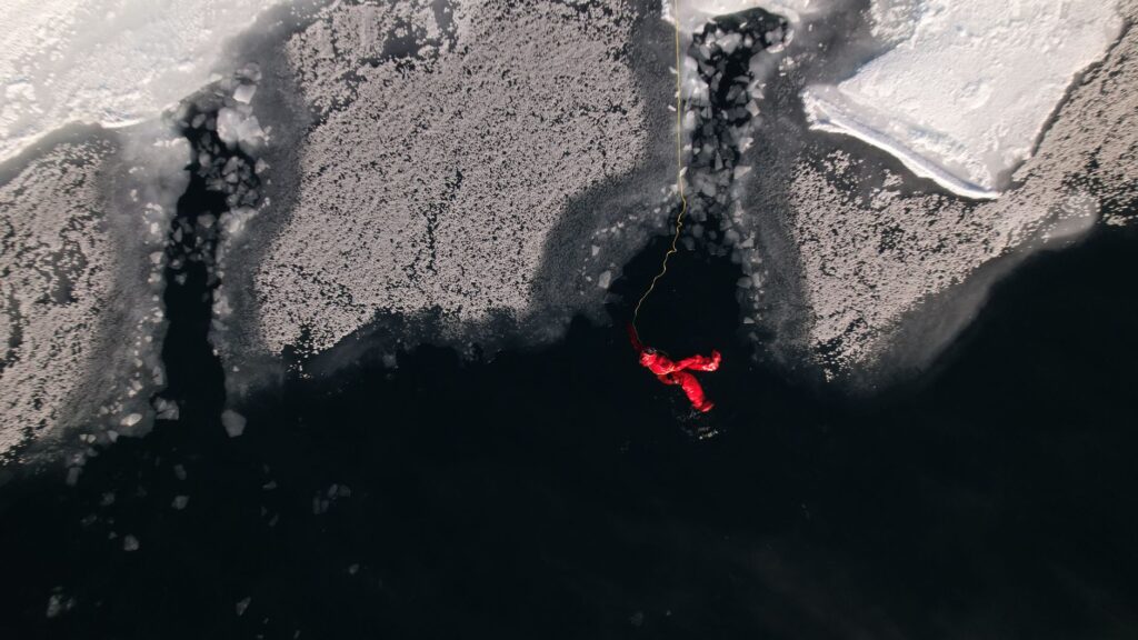 Aerial shot of a man in a red rescue suit on icy waters, tethered for safety.
