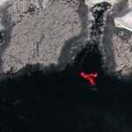 Aerial shot of a man in a red rescue suit on icy waters, tethered for safety.