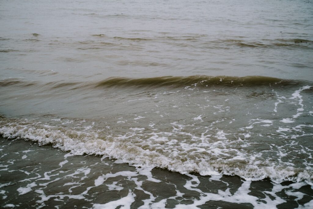 Gentle sea waves with seafoam crashing calmly on a sandy shore.