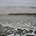 Gentle sea waves with seafoam crashing calmly on a sandy shore.