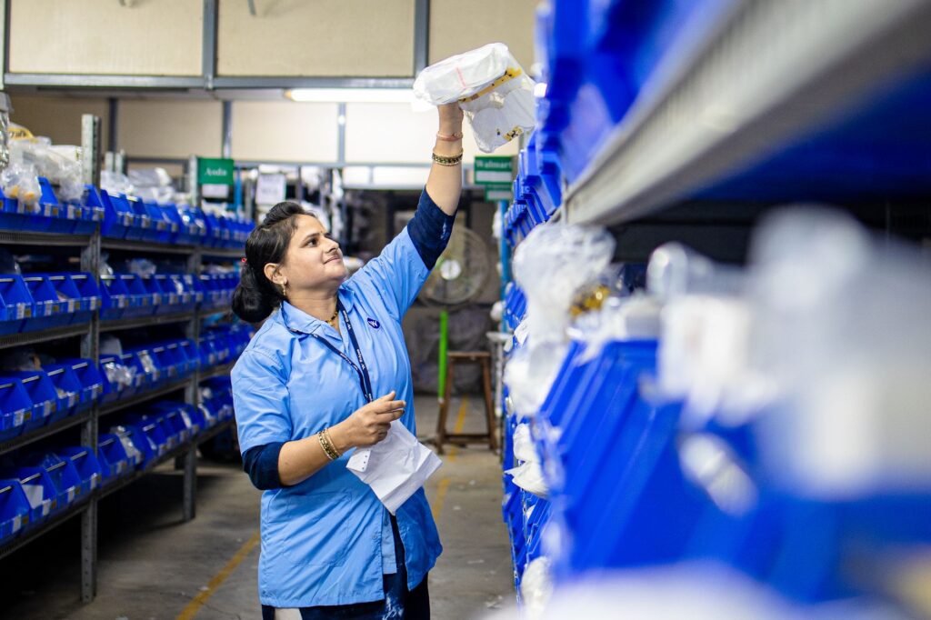 Female warehouse worker organizing inventory on blue industrial shelves. Efficient logistics management.
