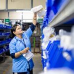 Female warehouse worker organizing inventory on blue industrial shelves. Efficient logistics management.