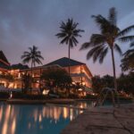 Luxurious tropical resort with swimming pool and palms at dusk, perfect for a tranquil vacation.
