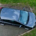 Top view of a black car parked on a grass and concrete surface, showcasing its exterior design.