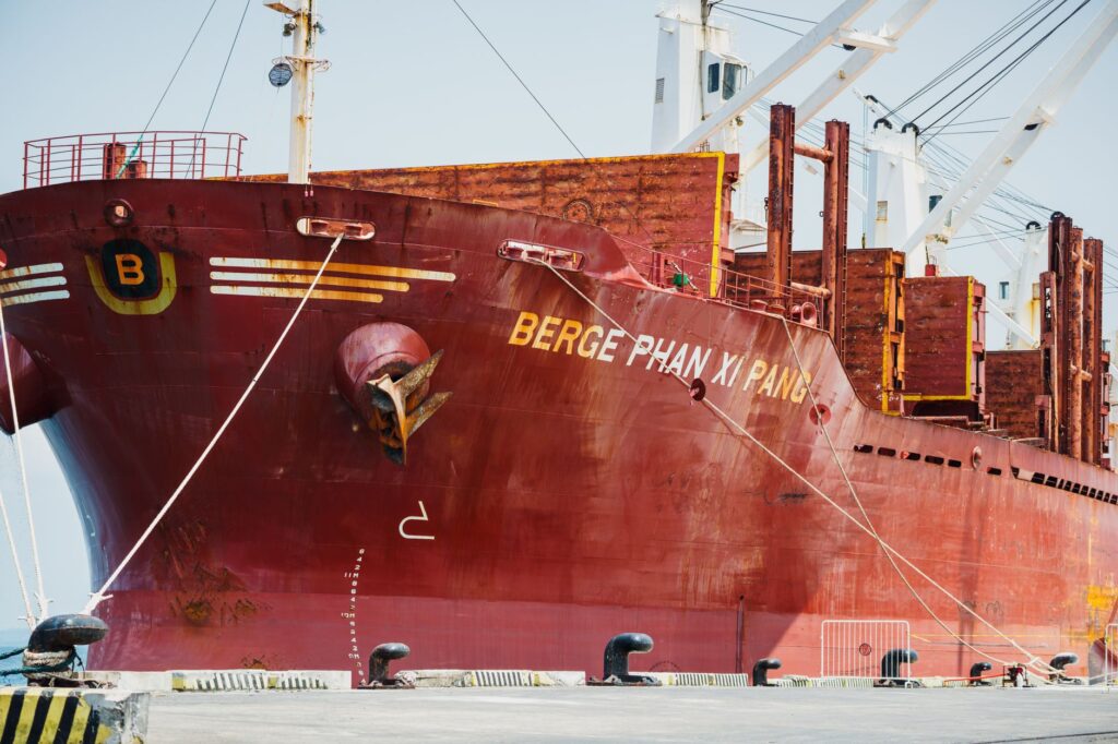 Close-up view of a large red cargo ship named Berge Phan Xi Pang docked at a port.