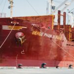 Close-up view of a large red cargo ship named Berge Phan Xi Pang docked at a port.