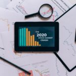 Flat lay of tablet showing 2020 stock market crash with charts and papers.
