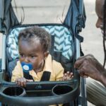 Father interacts with baby in stroller outdoors; a moment of bonding and care.