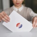 A person casting a vote by placing a ballot into a ballot box, symbolizing democratic participation.