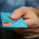 A close-up shot of a hand offering a blue debit card for payment.