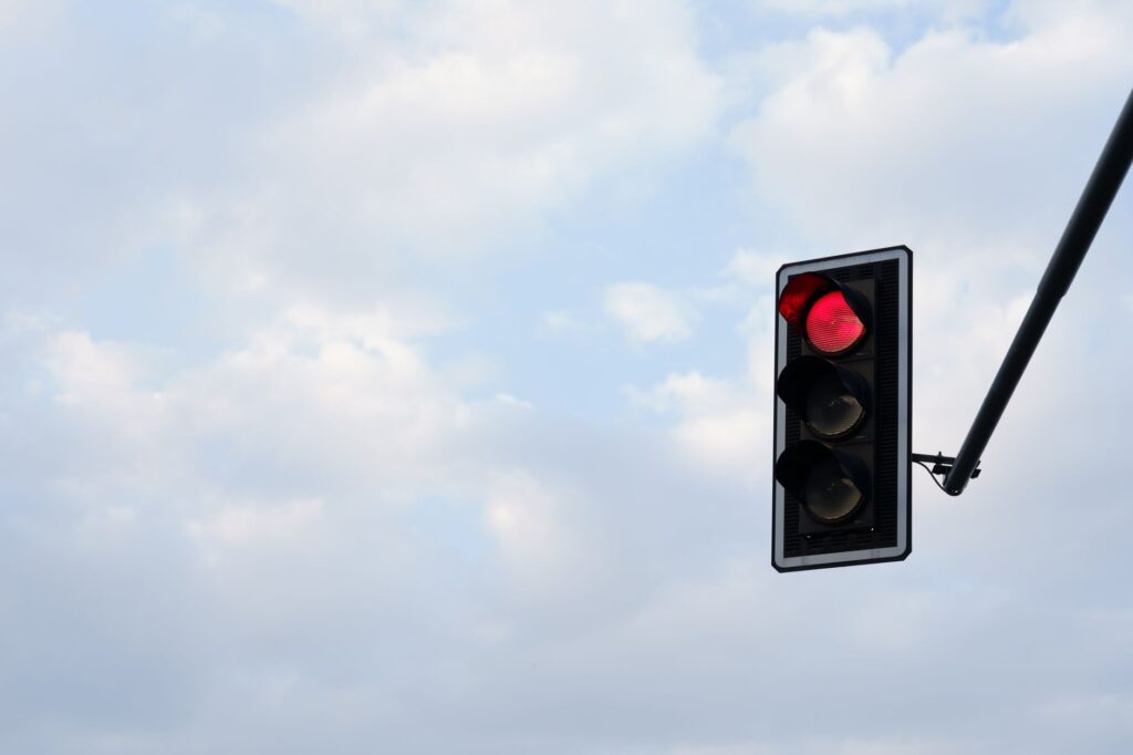 Red traffic light set against a bright, cloudy sky. Perfect for themes of travel, technology, and safety.
