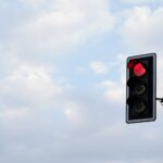 Red traffic light set against a bright, cloudy sky. Perfect for themes of travel, technology, and safety.