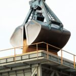 Clamshell grab unloading bulk cargo at an industrial port terminal.