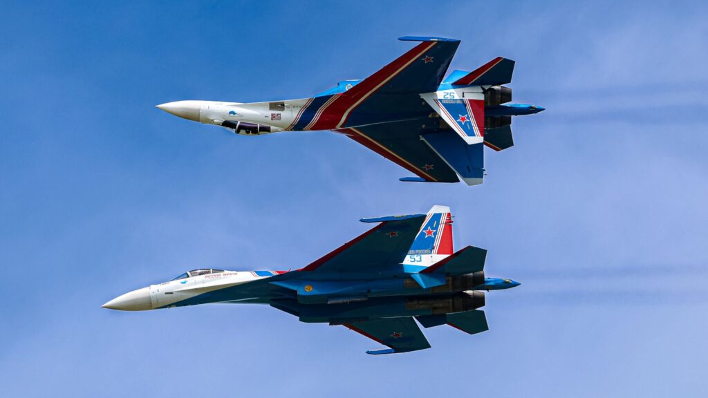 Two Sukhoi Su-27 fighter jets flying in close formation in a clear blue sky.