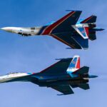 Two Sukhoi Su-27 fighter jets flying in close formation in a clear blue sky.