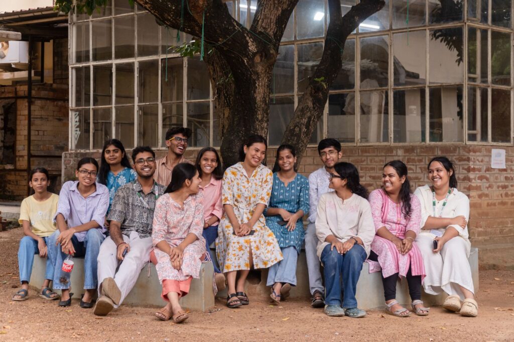 A group of college students smile and relax under a tree at a campus in Santiniketan, India.