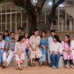 A group of college students smile and relax under a tree at a campus in Santiniketan, India.