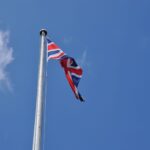 Union Jack flag waving on a flagpole against a clear blue sky in London, UK.
