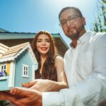 Happy couple proudly holding a miniature house symbolizing new homeownership.