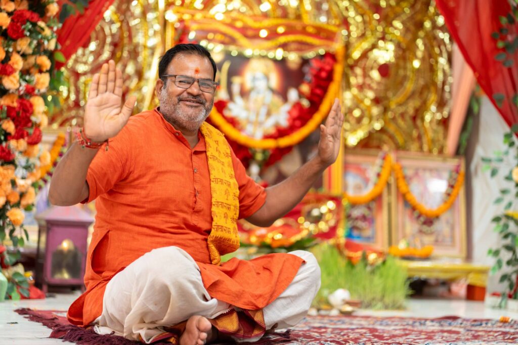 Smiling Indian man in traditional attire participating in a Hindu ceremony with vibrant decor.