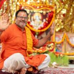 Smiling Indian man in traditional attire participating in a Hindu ceremony with vibrant decor.