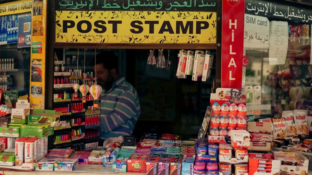 Colorful street kiosk showcasing an assortment of products and snacks with a vendor inside.
